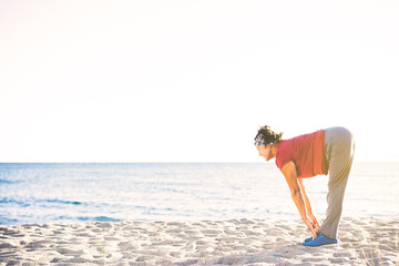 Fototapeta premium Senior woman exercising at the beach. Touching her toes, stretching
