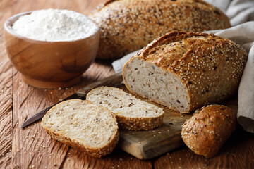 Rustic whole grain bread on a cutting board and bowl of flour on a wooden kitchen table