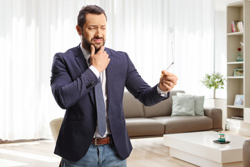Doubtful young man holding a cigarette in a living room