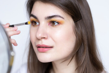 Young beautiful woman applying her colorful yellow eye make up with fluffy brush 