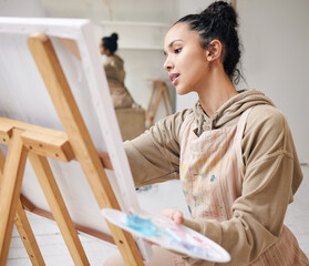 From her mind to the canvas. High angle shot of an attractive young woman painting on a canvas in...