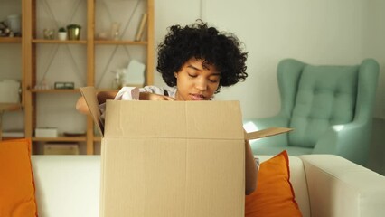 African girl unpacking delivery looking in box. Happy woman opening carton box. Female getting parcel looking at delivered goods items. Satisfied client positive feedback quick express deliver