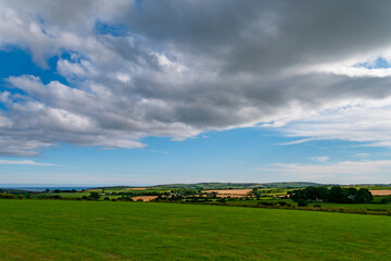 A grey cumulus cloud in the sky over the Irish countryside in summer. Irish landscape. Green farm...