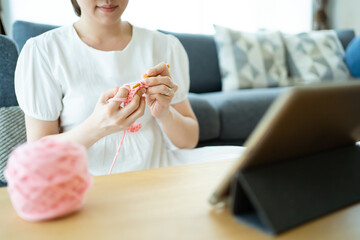 Happy cheerful Asian woman doing a crochet in living room in free time.