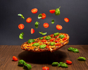 Pizza Margherita with basil tomato and mozzarella levitating over a wooden surface.