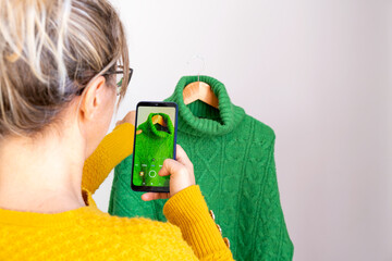 woman with phone in hand, taking photos of used clothes to sell in second-hand app, horizontal 
