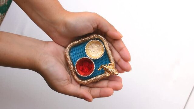 Hand holding beautiful small pooja thali having God Ganesh face, red roli and chawal means tika and rice in white background. It is used for any hindu festival like Rakshbandhan, diwali, durga puja.
