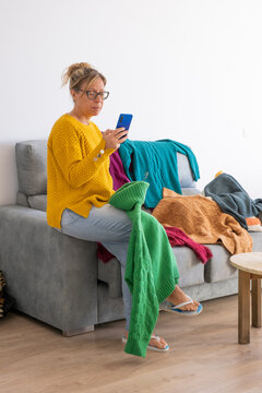 woman with glasses uploading photos of clothes to clothing app to sell from home
