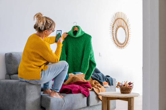 blonde woman taking photos of clothes to sell through used clothing application from her home
