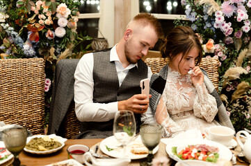 a young groom with a beard and a satisfied bride are sitting at the wedding table at a banquet. wedding couple at the banquet. festive food on the wedding day
