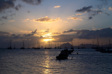 Fototapeta na wymiar Sunset panorama at the beach of Saint Anne in the south of french overseas island Martinique. Sailing boats anchoring in the bay near “Le Marin“, a popular spot for yachtsmen in the Caribbean sea.