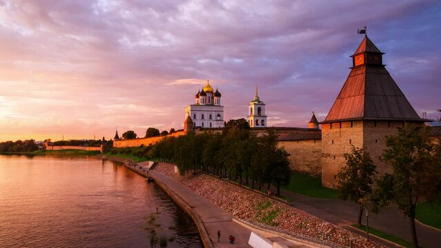 Pskov, Russia. Illuminated Pskov Kremlin at sunset. Popular landmark in Russia. Time-lapse of a colorful sky over a river and promenade area