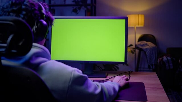 A monitor with green chroma key screen on the background of a young man playing virtual online games