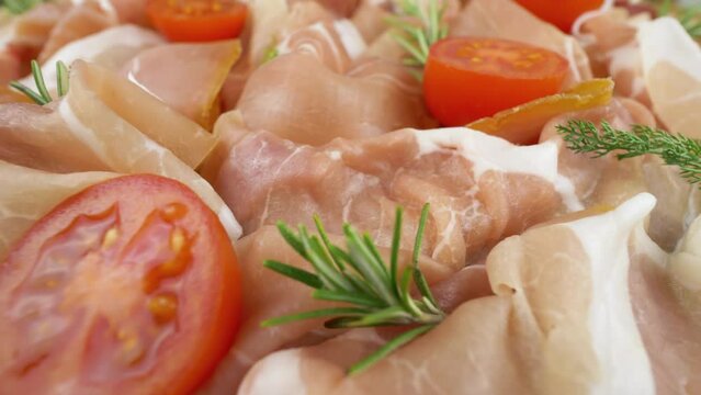 Raw ham. Seasoned air-dried cured meat, close-up. Prosciutto crudo with tomatoes and fresh rosemary