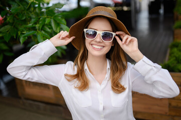 Young happy woman in summer clothes, sunglasses, straw hat posing on nature background, taking a selfie portrait. Summer, technology concept