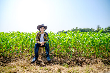 A female Asian farmer wearing a striped top and hat is sitting happily watching the corn crop.