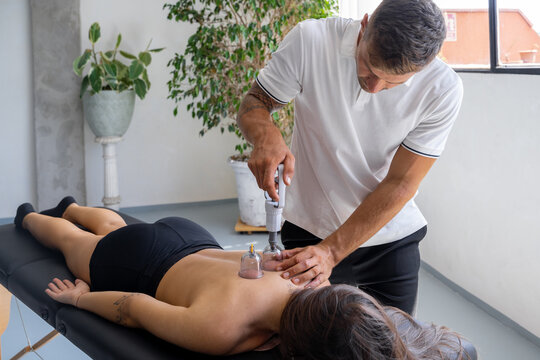 Male therapist treating back of female client with cupping massage