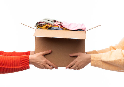 charity, donation and volunteering concept - hands holding cardboard box with clothes isolated on white background