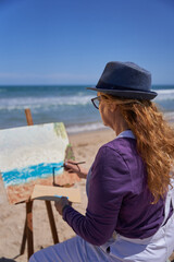 Lady painting a picture on the sand of the beach