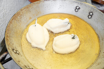 Three stuffed and battered poblano chilli peppers are being fried in a big metallic pan