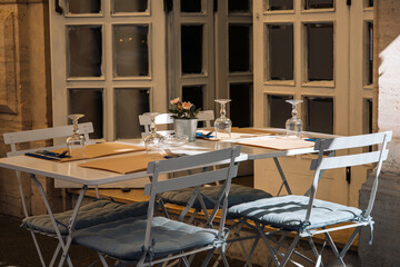 Outdoor empty coffee and restaurant terrace with white tables, vintage chairs and wine glasses in Europe. Cafe terrace on the pedestrian street in Rome, Italy. A set table is waiting for customers.
