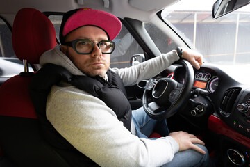 The man with glasses and cap driving car