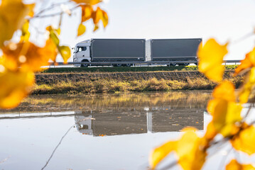 Truck goes on the road in autumn. car transport . Truck with semi-trailer in gray color.  Transport truck drives in autumn by the lake.