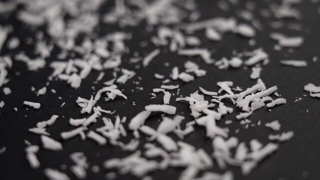 White coconut flakes sprinkling on a black surface in slow motion. Macro shot. Rotation