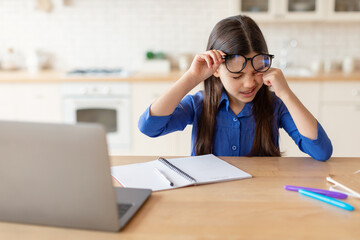 Schoolgirl Rubbing Sore Eye Using Laptop Wearing Glasses At Home