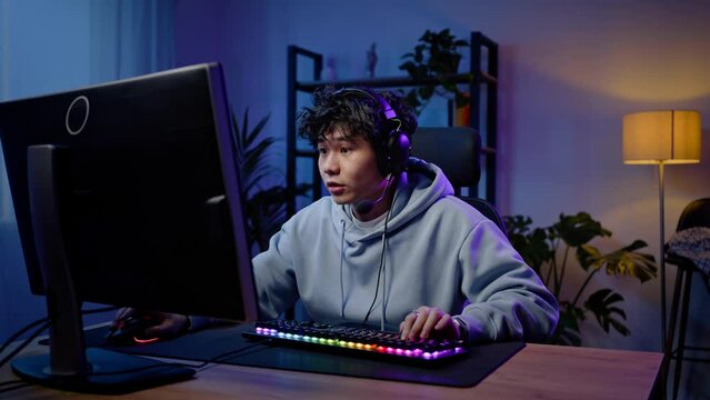 Young Asian man prof gamer playing video game with winner expression at gaming room. Slow motion