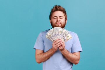 Portrait of satisfied bearded man smelling earned dollar banknotes, enjoying success and big...