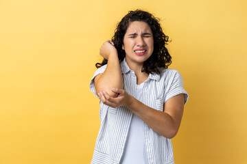 Portrait of woman with dark wavy hair having trauma after car accident, feels pain in elbow,...