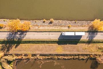 Plakat Truck goes on the road in autumn. car transport . Truck with semi-trailer in gray color. Transport truck drives in autumn by the lake.
