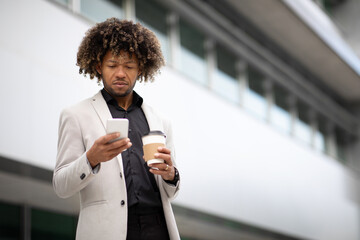 African american middle aged male entrepreneur holding takeaway coffee and using cellphone while walking outdoors