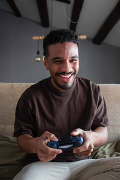 Cheerful ethnic man playing video game on bed