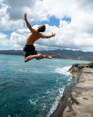 Man cliff jumping off Spitting Cave on Oahu, Hawaii. High quality photo
