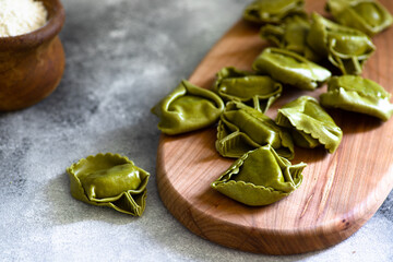 Homemade Italian tortellini with ricotta and spinach served on a wooden cutting board. A dish of classic Italian cuisine. Tortelloni di ricotta e spinaci. Close-up, selective focus