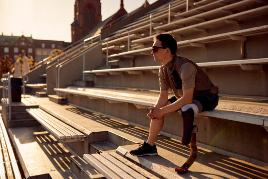 Man with a prosthetic running blade sitting on stadium bleachers