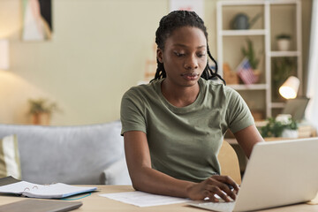 African American young woman working online on laptop sitting at table in the living room