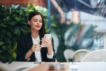 Stylish woman blogger sits in a cafe with a phone in her hands reads a message, mobile communication and internet abroad, video call, freelance work online