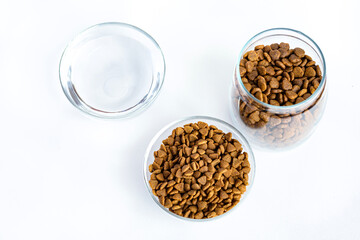 Dry pet food in a glass jar, bowl and water close-up on a white background. View from above