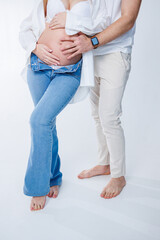Happy married couple. Pregnant woman and loving man hugging her belly on white background. Sensation of movement of the baby as a couple on the belly of the pregnant woman.