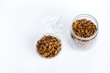 Dry pet food in a glass jar and bowl close-up on a white background. View from above