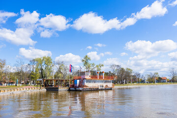 Fototapeta premium Tranquil summer day in Palic Nature Park, Serbia. Colorful clouds decorate a beautiful blue sky above a picturesque lake and lush landscape - an inspiring destination for holiday relaxation.
