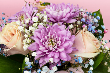 Beautiful bouquet of roses, chrysanthemums, and multicolored gypsophila close-up on a pink background.