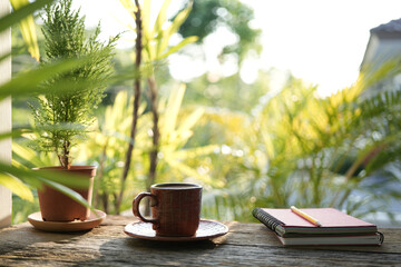 spiral notebook and wooden coffee cup on wooden table with greenery scene