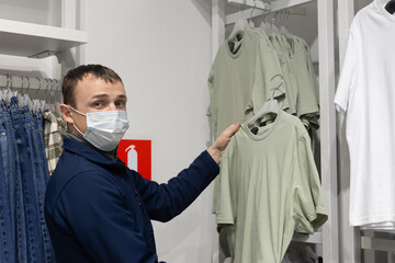 Fototapeta na wymiar A man in a protective face mask chooses casual clothes. Retail trade. Consumerism