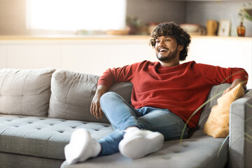 Domestic Rest. Smiling Young Indian Man Relaxing On Sofa In Living Room