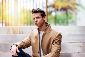 Portrait of stylish handsome young man with coat sitting outdoors