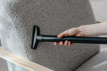 Woman vacuums modern armchair with soft upholstery, closeup view